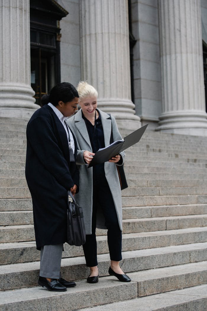 Two diverse professionals reviewing documents on courthouse steps, symbolizing cooperation.